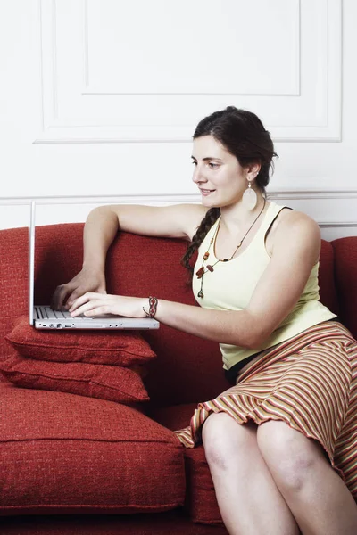 Side profile of a young woman sitting on a couch and using a laptop