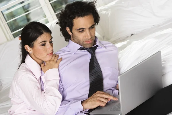 Close-up of a businessman and a businesswoman sitting on the bed using a laptop