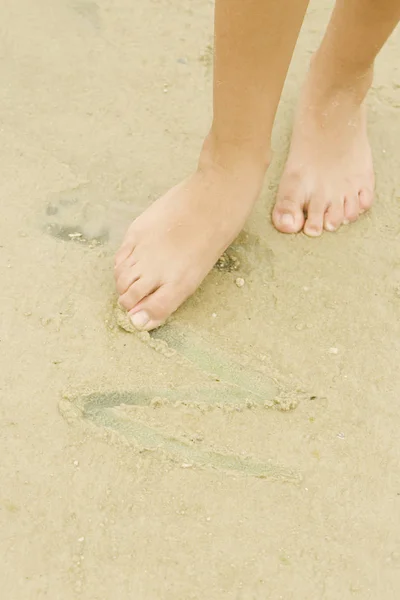 Low section view of a woman drawing in sand with her toe