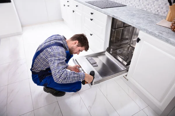Jovem Reparador Fixando Máquina Lavar Louça Com Broca Elétrica Cozinha — Fotografia de Stock