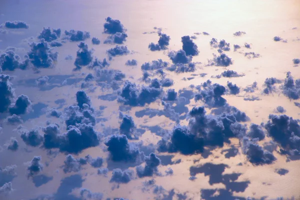 Beautiful view from window of plane flying over clouds and sea surface. Natural panorama with clouds. White clouds moving above water surface of sea. Landscape with sun reflected in sea surface