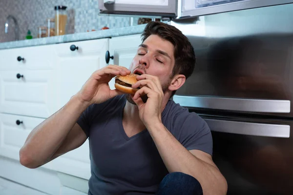 Close Man Eating Burger Leaning Refrigerator — Stock Photo, Image