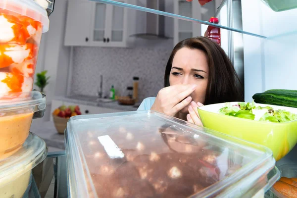 一个女人在一个开放的冰箱里拿着鼻子接近肮脏的食物 — 图库照片