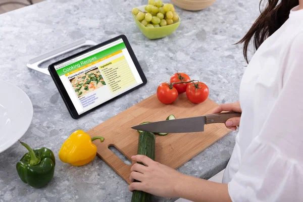 Woman Cutting Cucumber With Kitchen Knife Near Cooking Recipes On Digital Tablet Screen