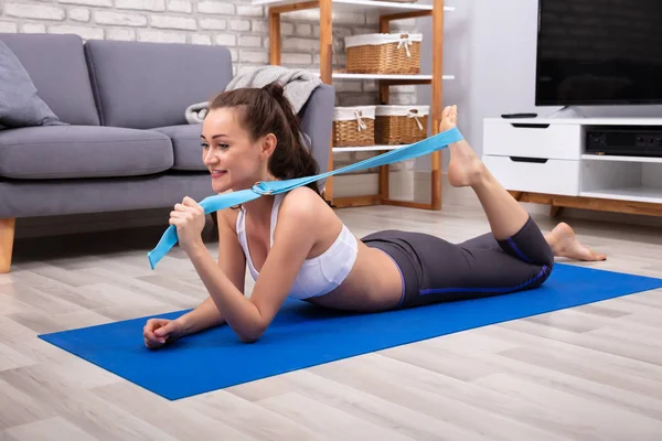 Glad Ung Kvinde Sportstøj Gør Træning Med Yoga Bælte Hjemme - Stock-foto