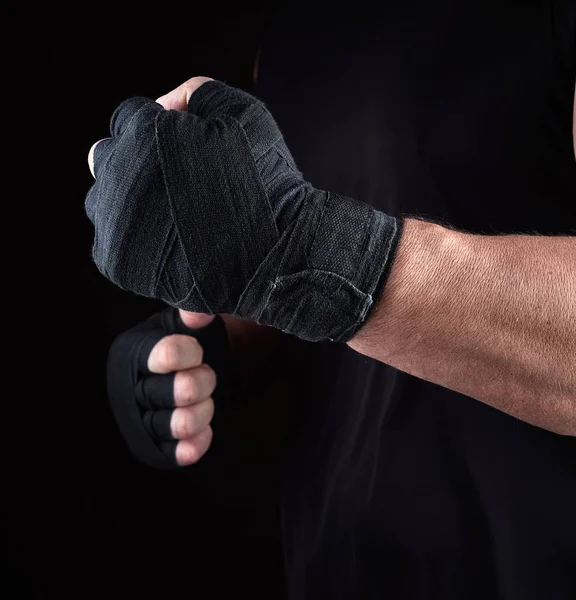 athlete stands in a fighting stance, his hands wrapped in black textile bandage