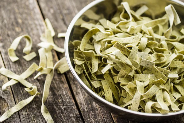 Raw italian pasta. Dry noodles with spinach in bowl.