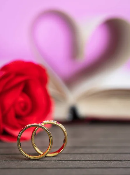 结婚戒指书页的书弯曲成一个心脏形状和红玫瑰 爱的概念的心形状从书页 — 图库照片