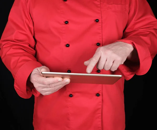 彼の手に電子タブレットを持っている赤い制服のシェフと画面に触れ 黒の背景 — ストック写真