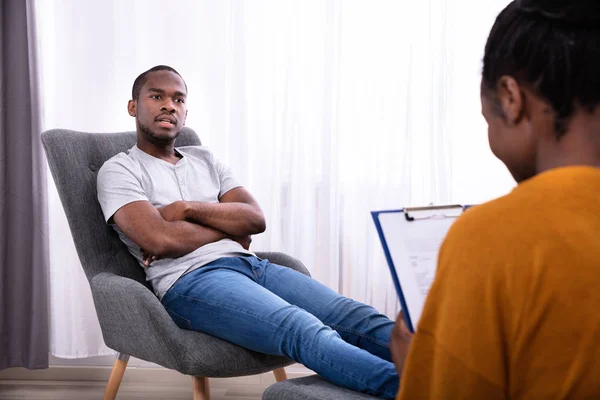 Junger Afrikanischer Mann Sitzt Auf Stuhl Neben Psychologin Mit Klemmbrett — Stockfoto