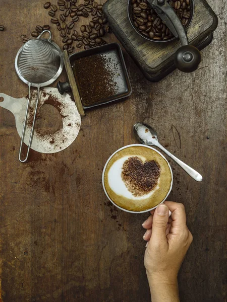 コーヒー豆 グラインダーと完成したカップを持っている女性の手の厄介な素朴な木製のテーブルの写真 — ストック写真