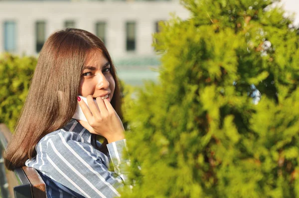 美しい緑の空間の近くの都市公園で電話で話す若い女の子の美しい肖像画 — ストック写真