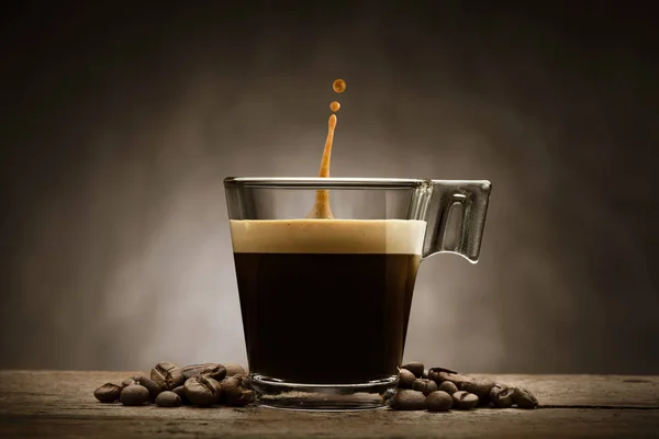 Schwarzer Kaffee Glasschale Mit Kaffeebohnen Und Springtropfen Auf Holztisch — Stockfoto
