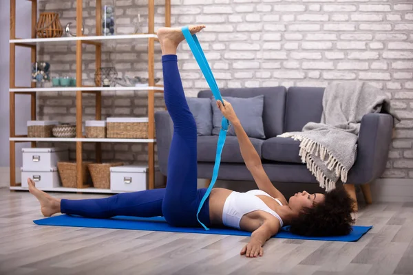 African Young Woman Doing Stretching Exercise With Yoga Belt While Doing Exercise On Fitness Mat
