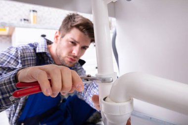 Young Male Plumber Repairing Sink Pipe With Adjustable Wrench clipart