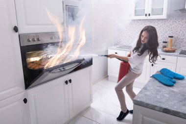 Woman Using Fire Extinguisher To Stop Fire Coming Out From Oven In Kitchen clipart
