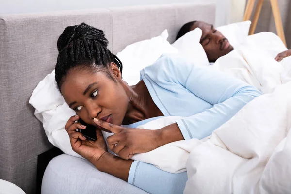 Mladá Africká Žena Mluví Mobilu Zatímco Její Manžel Spí Posteli — Stock fotografie