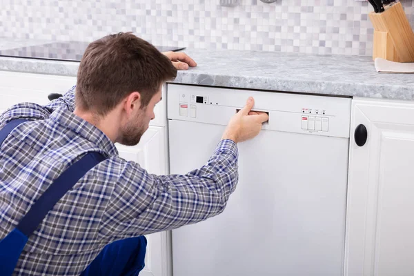 キッチンで食器洗い機のボタンを押す若いサービスマン — ストック写真