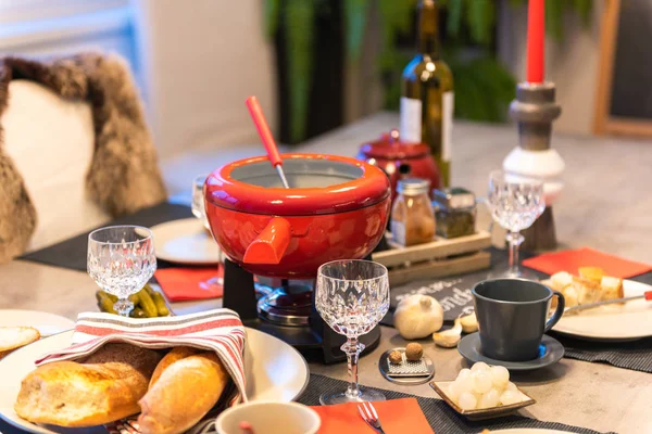 Traditional swiss cheese fondue in a red pot on concrete dining table.