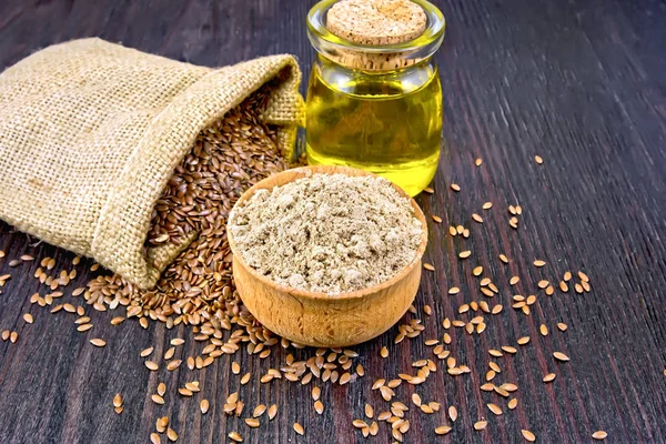 Flax flour in a bowl, seeds in a bag and linen oil in a glass jar on a background of a dark wooden board