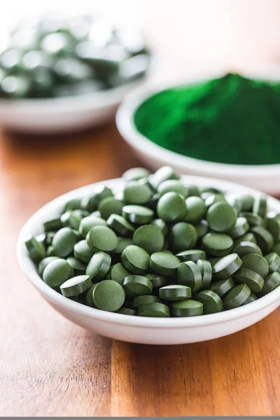 Green chlorella pills or green barley pills in bowl.