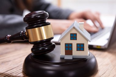 House Model With Gavel In Front Of A Businessperson Using Laptop On Wooden Desk clipart