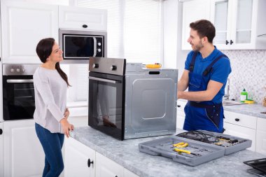 Smiling Repairman Repairing Oven On Kitchen Worktop In Front Of Woman clipart