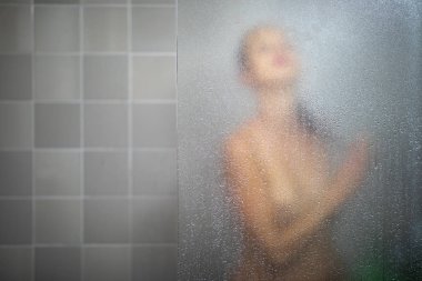 Woman taking a long hot shower washing her hair in a modern design bathroom clipart