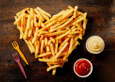 Heart shaped serving of French Fries with dips, dressings or sauce in small bowls alongside on wood clipart