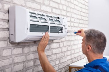 Mature Male Technician Fixing Air Conditioner With Screwdriver clipart