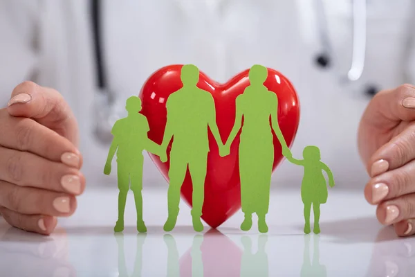 Рука Доктора Защищает Зеленую Семейную Бумагу Вырезанную Красным Сердцем Столе — стоковое фото