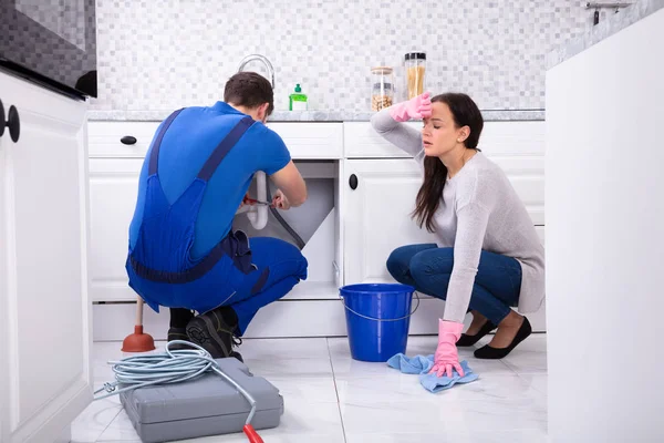 Man Loodgieter Repareren Spoelbak Pijp Terwijl Vermoeide Vrouw Schoonmaken Vloer — Stockfoto