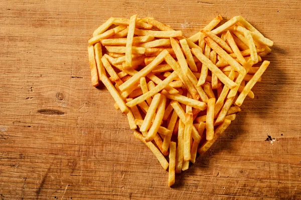 Close-up view from above of a heart shape made of tasty French fries served on a wooden rustic table as concept for love or fast food