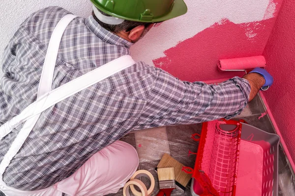 白で白人の家画家ワーカー作業のオーバー オール ローラーで彼がピンクの着色された絵画で壁塗料します 建設業界 トップ ビュー — ストック写真