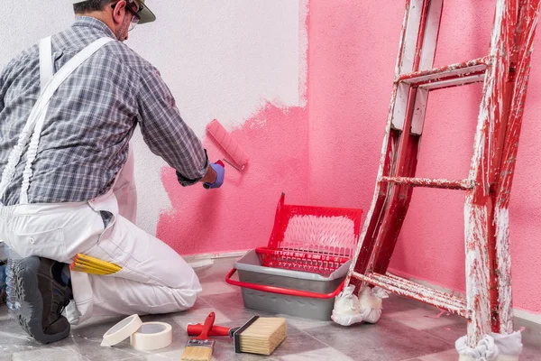 白で白人の家画家ワーカー作業のオーバー オール ローラーで彼がピンクの着色された絵画で壁塗料します 建設業界 作業の安全性 底面図 — ストック写真
