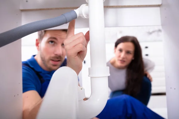 Jovem Encanador Masculino Mostrando Danos Tubulação Dissipador Para Mulher Casa — Fotografia de Stock