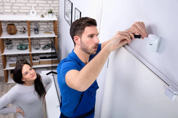 Glückliche Frau Beim Anblick Eines Elektrikers Der Bewegungsmelder Der Wand — Stockfoto