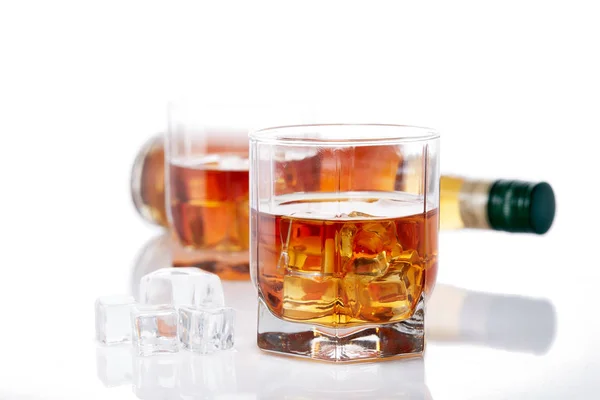 ウイスキーのボトルと反射して白い背景に氷とウイスキーの2つのグラス — ストック写真