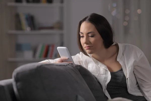 一个疲惫的女人在家里的夜晚坐在沙发上查看智能手机内容 — 图库照片