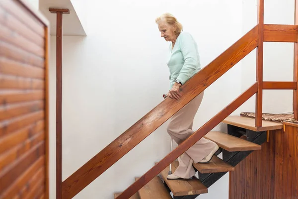 Elderly woman at home using a walking cane to get down the stairs