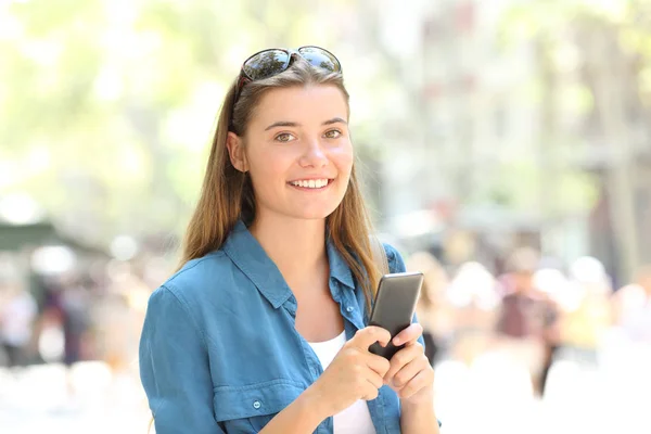 Fashion happy girl holding a smart phone looks at you in the street