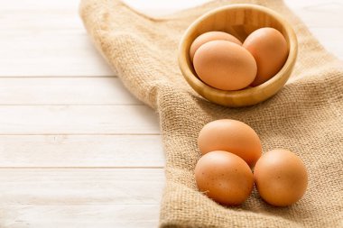 Raw chicken yellow eggs in a wood bowl on a wooden background. Healphy eating concept. Top view and copy space clipart