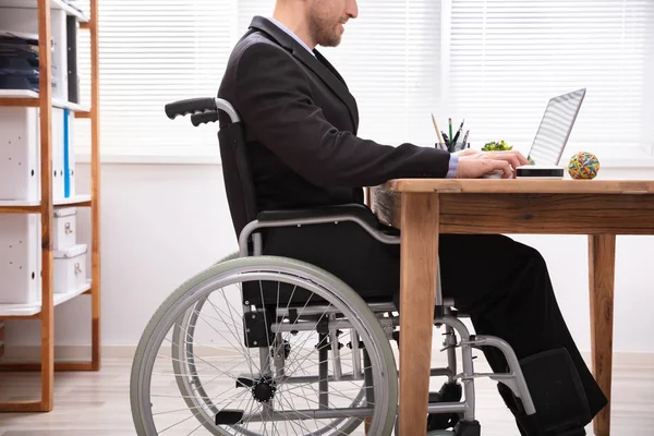 在工作场所使用笔记本电脑坐在轮椅上的残疾商人 — 图库照片