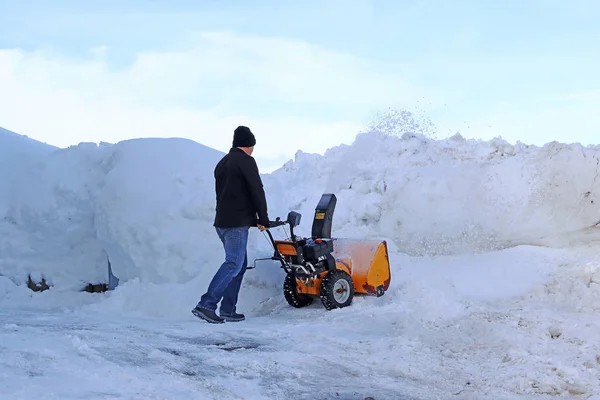 A man with a snow blower clears high snow