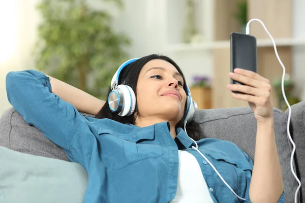 在家里客厅的沙发上 坐在智能手机上听音乐的松懈女人 — 图库照片