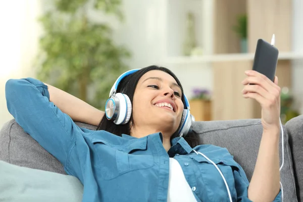 一个快乐的女人坐在客厅的沙发上 听着智能手机里的音乐 — 图库照片