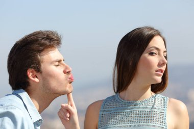 Woman rejecting a friend kiss in a sunny day clipart