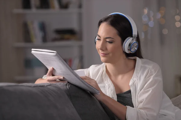 一个带着耳机的认真的学生晚上在家里的沙发上读书 — 图库照片