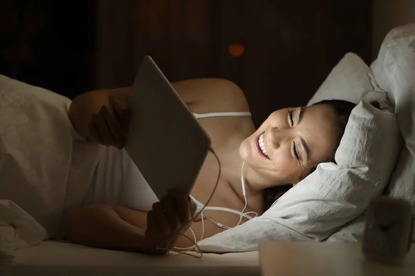 Happy woman watching movie on a tablet in the night on a bed at home