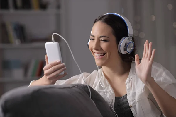 一个快乐的女人 晚上在家里坐在沙发上 带着耳机和智能手机打一个视频电话 — 图库照片